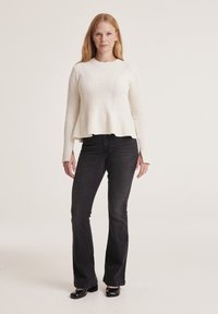 White knitted sweater with ribbed texture and a flared hem, paired with black flared jeans and black shoes.