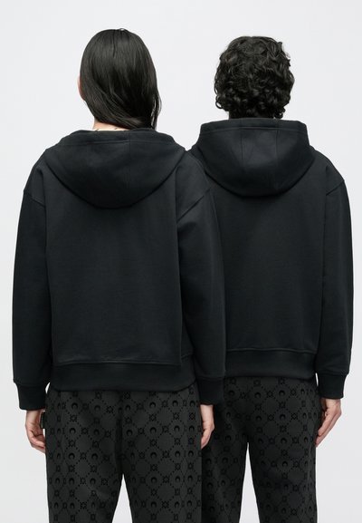Sweatshirts pretos com capuz e corte descontraído, com bainhas caneladas e um bolso canguru, combinados com calças pretas estampadas exibindo um design subtil.