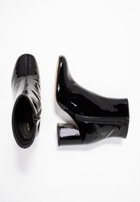 Black patent ankle boots with a chunky heel, featuring a side zipper, smooth texture, and pointed toe design.