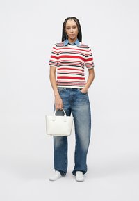 Κομμάτι πλεκτής πουκάμισας πόλο με ρίγες σε κόκκινο, λευκό και ναυτικό μπλε, μπλε τζιν παντελόνι και λευκή τσάντα tote. Το μοντέλο φοράει λευκά αθλητικά παπούτσια και έχει πλεγμένα μαλλιά.