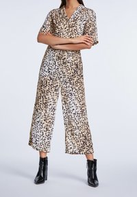 Combinaison à imprimé léopard beige et noir, confectionnée dans un tissu léger. Elle présente des manches courtes, un col et un pantalon à jambes larges.