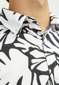 Kurzarmhemd in Schwarz und Weiß mit einem mutigen abstrakten Muster. Hergestellt aus leichtem Stoff mit Kentkragen und sichtbarem Knopfdetail.