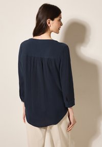 Blusa creata blu navy in tessuto stropicciato con scollatura rotonda, maniche tre quarti con polsini abbottonati e design della schiena leggermente arricciato.