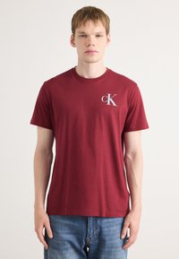 Bordó T-shirt, pamutből készült, kereknyakú, bal mellen egy kis fehér "cK" logóval, rövid ujjú.
