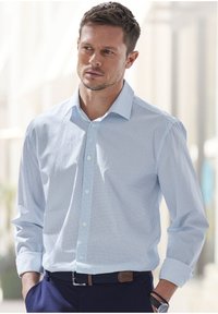 Camicia azzurra chiaro con un piccolo motivo geometrico, maniche lunghe, colletto rotondo e polsini arrotolati, abbinata a pantaloni scuri.