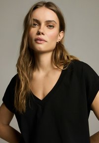Czarna koszulka z dekoltem w serek, z krótkim rękawem i luźnym krojem, prezentowana na neutralnym tle. Gładka tekstura materiału.