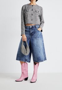 Karo zkrácená bunda se dvěma kapsami, modré džínové culottes, růžové kovbojské boty a texturovaná kabelka v černobílé barvě.