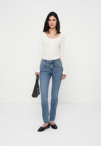 Κολάν τζιν σε ανοιχτό μπλε ντένιμ, σε συνδυασμό με εκρού μακρυμάνικη μπλούζα. Τσάντα με ασπρόμαυρο πουά σχέδιο στο χέρι, με μαύρα ίσια παπούτσια.