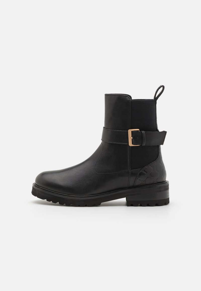 Botas negras de tobillo con parte superior de cuero suave, paneles laterales elásticos, una hebilla decorativa y un talón texturizado. Suela de goma robusta.