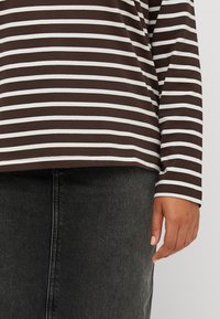 Top de manga larga a rayas marrón y blanco con un corte holgado. Material de algodón suave. Combinado con una falda negra lisa. Diseño minimalista.