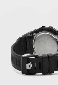 Reloj de goma negra con correa texturizada, fondo de acero inoxidable y herrajes plateados. Presenta un diseño audaz y robusto.