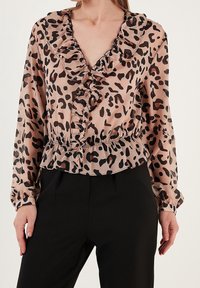 Blusa in stampa leopardata in morbido tessuto, con scollatura a V arricciata, vita elasticizzata e maniche lunghe con polsini. Schema di colori: beige, marrone, nero.