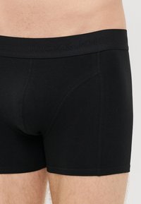 Sorte bomullsboxer med et merket elastisk liv, med en tett passform, sømløse sider og en strukturert frontlomme.