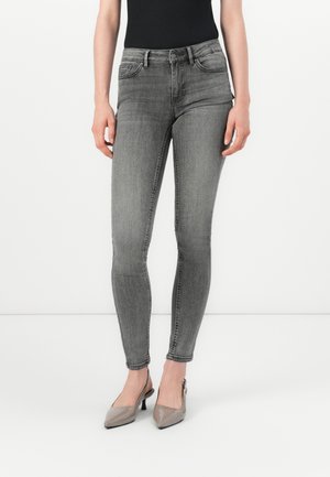 Jean skinny gris en denim, avec un design classique à cinq poches et une légère décoloration. Associés à des talons slingback en cuir verni.