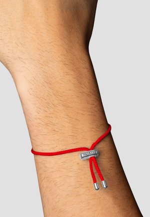 Rød flettet snorearmbånd med sølvhardware fastgjort i midten, der har to metalender og en flad charm indgraveret med "NIALAYA."