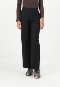 Black wide-leg pants made from a sturdy fabric, featuring a front button closure and side pockets. Paired with gray athletic shoes.