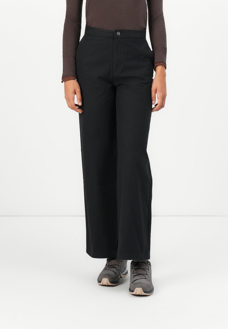 Black wide-leg pants made from a sturdy fabric, featuring a front button closure and side pockets. Paired with gray athletic shoes.