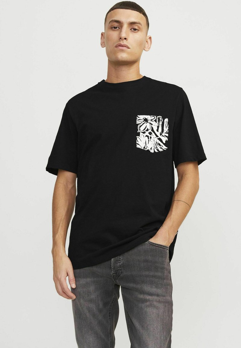 Camiseta de algodón negra con un bolsillo estampado en blanco con flores, mangas cortas y un corte relajado, combinada con jeans de mezclilla grises.