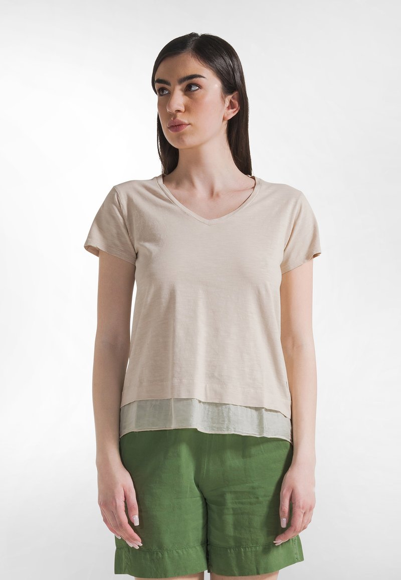 Camiseta beige con escote en V y manga corta, dobladillo en capas de color verde claro, hecha de tela suave. Combinada con pantalones cortos verdes.