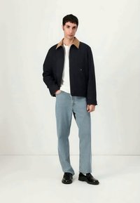 Námornícky skrátený kabátik s hnedým golierom, biela košeľa a svetlomodré rovné džínsy; čierne topánky. Hladká látka, jednoduchý dizajn a neutrálné tóny.