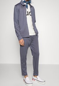 Light blue, cotton-blend jacket over a white t-shirt with black text, paired with matching joggers and white slip-on shoes with colored accents.