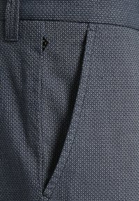 Pantalons à motif navy en tissu texturé, dotés d'une poche latérale et d'une petite étiquette logo noire près de la taille.