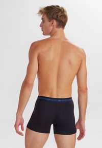 Black boxer shorts with a blue waistband logo, fitted design, smooth texture, and conventional cut, viewed from the back.