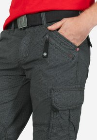 Cargo pants in dark gray fabric with a geometric pattern. Features include a zipper pocket, accent stitching, and a black waistband with a metal buckle.