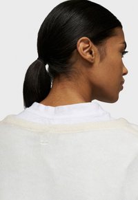 Maglione beige chiaro visto da dietro, caratterizzato da una consistenza morbida e una vestibilità comoda. Il collo è bianco e stratificato sotto.