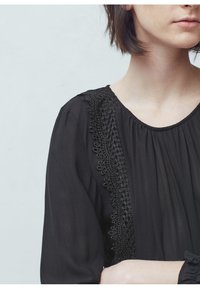 Blusa nera con scollo arricciato, caratterizzata da dettagli in pizzo intricati lungo la spalla e una morbida trama di tessuto fluido.