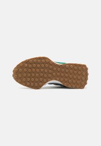 Suela de zapato deportivo con una superficie de goma texturizada marrón que presenta patrones circulares, acentos blancos y un borde superior negro y verde.