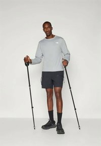 Sportieve outfit met een lichtgrijze lange mouw top en zwarte shorts, uitgerust met wandelstokken. Zwarte sneakers en sokken maken de look compleet.