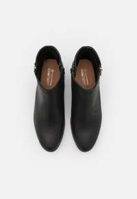 Ein Paar schwarze Lederstiefeletten mit seitlichen Reißverschlüssen, runden Zehen und braunen Innensohlen auf einem weißen Hintergrund.