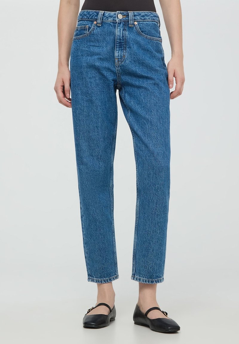 Niebieskie dżinsy z wysokim stanem i prostą nogawką, z zapięciem na guziki, pięcioma kieszeniami i delikatnymi przetarciami przy dolnej krawędzi.