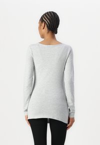 Langärmlige graue Tunika aus weichem Material, mit einem runden Ausschnitt und einem abgerundeten Saum, kombiniert mit schwarzen Leggings.