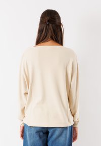 Maglione beige a maglia con una vestibilità comoda, scollatura ampia, maniche lunghe con polsini a coste e texture morbida, abbinato a jeans in denim blu.