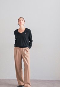 Top negro de manga larga con escote en V pronunciado y pequeño logo, combinado con pantalones anchos beige, ambos de una tela suave y fluida.