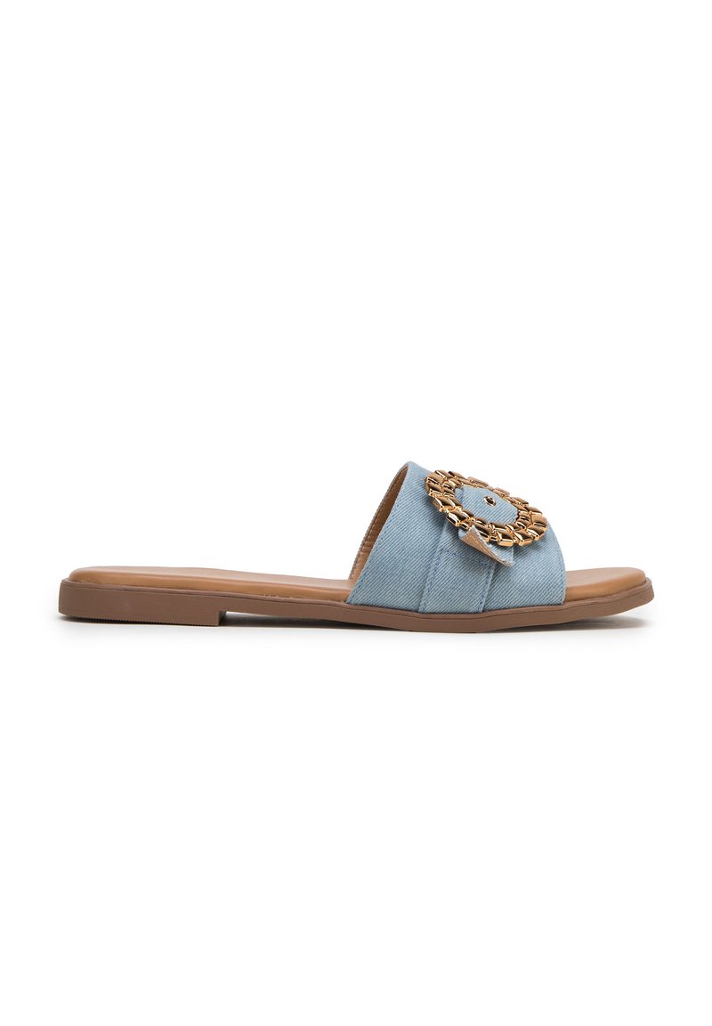 Sandalo in denim azzurro chiaro con suola piatta, caratterizzato da un dettaglio circolare in tonalità dorata sulla fascia superiore. Texture liscia e design aperto.