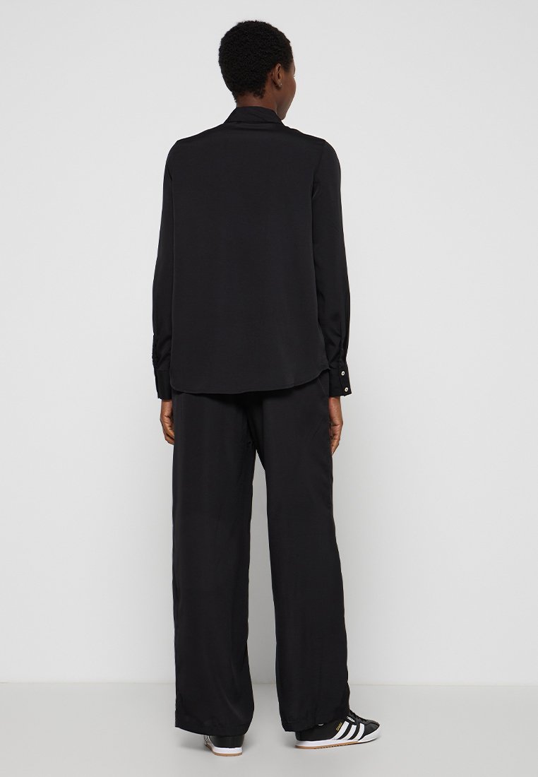 Zwarte blouse met lange mouwen en een relaxte pasvorm, met een soepele textuur en knoopaccenten op de manchetten, gecombineerd met bijpassende losvallende zwarte broeken.