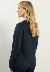 Granatowy sweter z dzianiny z długimi rękawami, o prążkowanej fakturze i okrągłym dekolcie. Boki mają rozcięcia, a luźny krój zwiększa komfort.