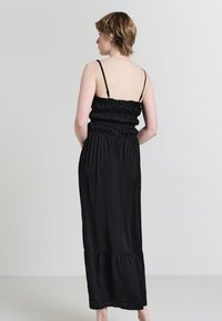 Schwarzes Maxikleid mit dünnen Trägern, elastischem, gerafftem Oberteil und ausgestelltem Saum. Weiches Material mit glatter Textur, geeignet für legere Anlässe.