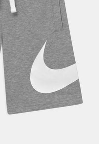 Šedé sportovní šortky vyrobené z měkké tkaniny. Obsahují velké bílé logo Nike a stahovací pás na šňůrku. Součástí jsou boční kapsy a hladký povrch.