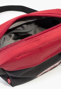 Bolsa com fecho vermelho e preto, feita de tecido durável, apresentando um exterior texturizado e um forro interior liso. Inclui um compartimento principal espaçoso.