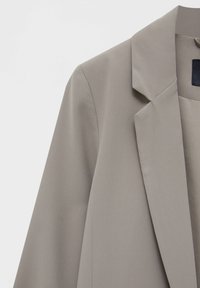 Jasnoszary żakiet o gładkiej teksturze, z wyciętymi klapami i dopasowanymi ramionami, charakteryzujący się eleganckim, minimalistycznym stylem.
