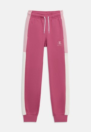 Pantalon de survêtement rose fuselé avec des panneaux latéraux rose clair et blanc, taille élastique avec cordons blancs et petit logo Champion sur la jambe gauche.