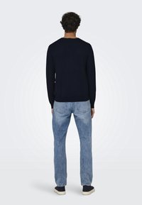 Pull bleu marine avec un col rond, associé à un jean bleu clair. Le jean présente un léger effet délavé et des poches arrière. Aucun motif ou logo visible.