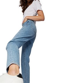 Vaqueros de color azul claro con cintura alta y diseño de pierna recta. La tela parece de mezclilla con texturas sutiles. Se ve parcialmente un zapato deportivo blanco.