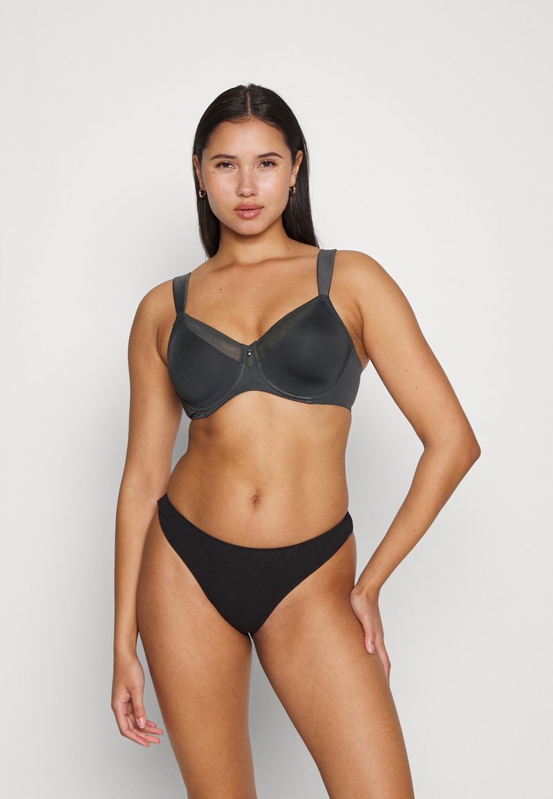 Czarny stanik z fiszbinami w ciemnoszarym kolorze, z przezroczystymi akcentami z siateczki, szerokimi ramiączkami i gładką miseczką. W komplecie z czarnym majtkami o wysokim kroju.