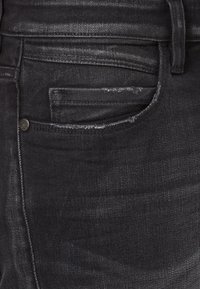 Czarne jeansy z denimu o klasycznym fasonie z pięcioma kieszeniami, z wyblakłą fakturą i metalowym guzikiem jako akcentem na przedniej kieszeni.