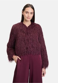 Veste courte bourgogne avec une surface texturée et shaggy. Présente des manches longues et un col simple. Associée à un pantalon ample assorti.